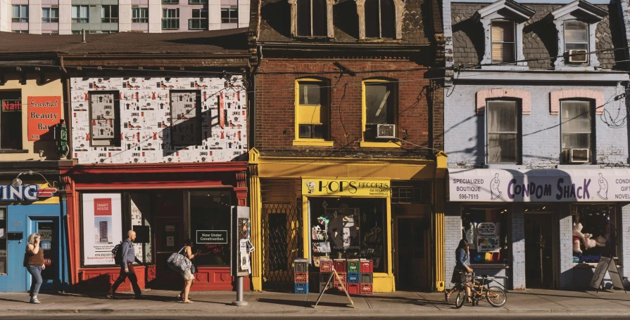 a group of people walking down a street next to tall buildings, by Carey Morris, pexels contest winner, old shops, toronto, yellow and red color scheme, bookshops