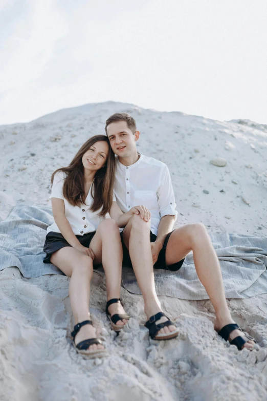 a man and woman sitting on a rock in the sand, wearing a linen shirt, dasha taran, low quality photo, multiple stories