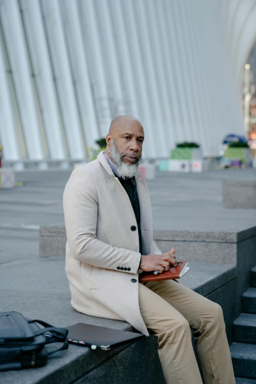 a man sitting on the steps of a building, an album cover, inspired by William H. Mosby, pexels contest winner, modernism, bald head and white beard, at new york fashion week, photo courtesy museum of art, standing in a city center