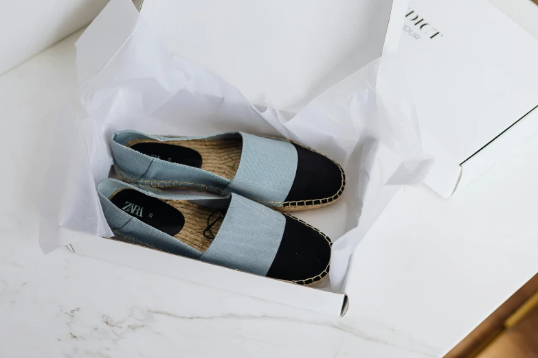 a pair of shoes in a box on a table, ice blue, with black, luca, flat grey