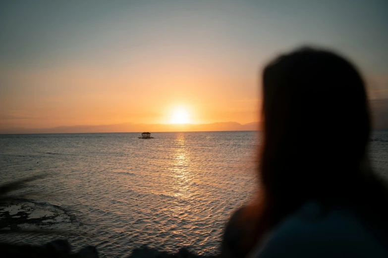 a woman watching the sun set over the ocean, a picture, pexels contest winner, split near the left, low quality photo, shot from a distance, distant expression