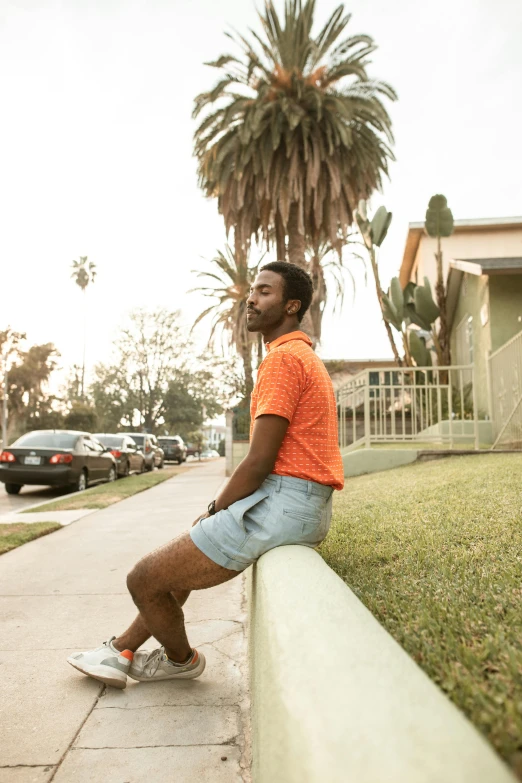 a man sitting on a curb in front of a house, by Carey Morris, trending on unsplash, wearing an orange t-shirt, with palm trees in the back, donald glover, lgbtq