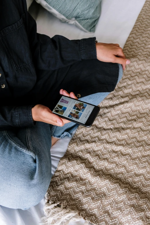 a person sitting on a bed holding a cell phone, a picture, wearing a dark shirt and jeans, like a catalog photograph, unsplash photography, multiple stories