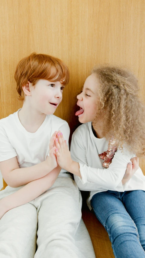 a couple of kids sitting on top of a wooden floor, by Arabella Rankin, pexels, earing a shirt laughing, ginger hair, reaching out to each other, white