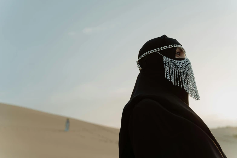 a person standing in the middle of a desert, an album cover, inspired by Hedi Xandt, pexels contest winner, hurufiyya, balaclava covering face, chain mail, hijab, still from the movie