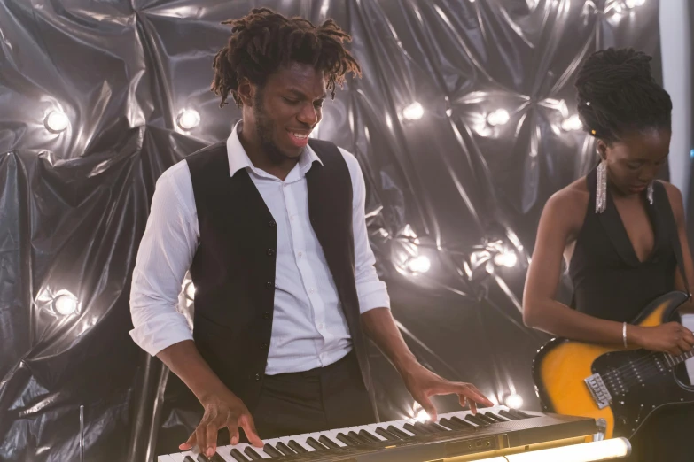 a man standing next to a woman in front of a keyboard, an album cover, pexels, maria borges, performing a music video, wide film still, band playing