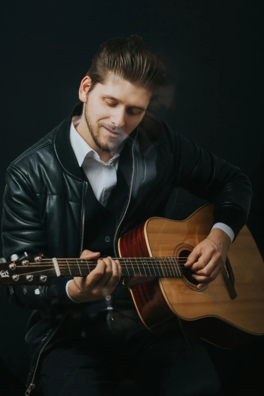 a man in a leather jacket playing a guitar, zachary corzine, professional modeling, slightly smiling, classical