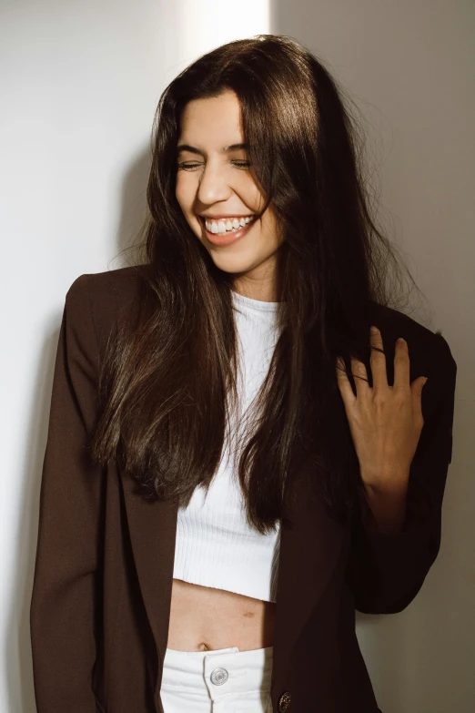 a beautiful young woman standing next to a white wall, trending on pexels, brown long and straight hair, mutahar laughing, jacket, promo image