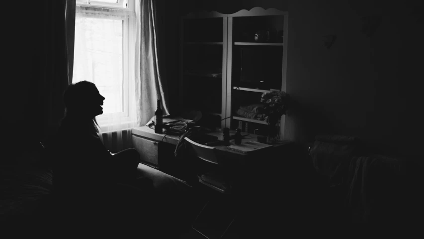 a woman sitting at a desk in front of a window, a black and white photo, inspired by Elsa Bleda, unsplash, romanticism, detailed silhouette, someone in home sits in bed, medium format. soft light, dark image