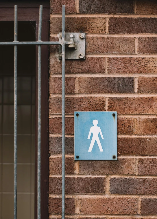 a blue sign on the side of a brick building, by Kristian Zahrtmann, trending on unsplash, humanoid figure, toilet, narrow footpath, diverse