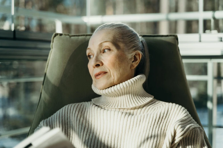 a woman sitting in a chair reading a book, by Winona Nelson, pexels contest winner, wearing turtleneck, elderly, pale complexion, instagram post