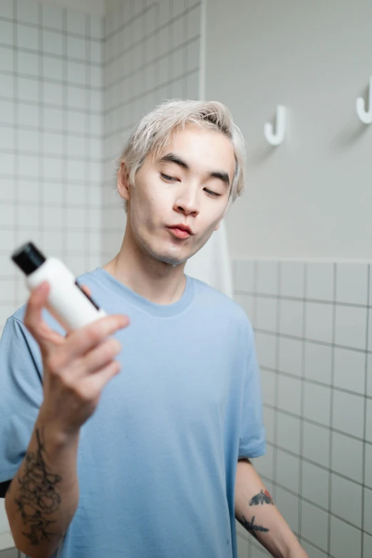 a man standing in a bathroom holding a bottle of lotion, by Jang Seung-eop, cloudy grey hair, ethnicity : japanese, non-binary, clean shaven wide face