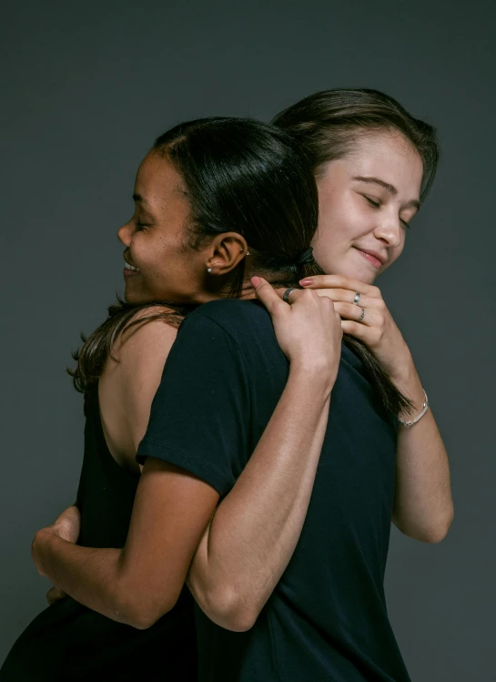 a couple of women standing next to each other, trending on unsplash, antipodeans, hugging and cradling, joey king, mixed race, promotional image
