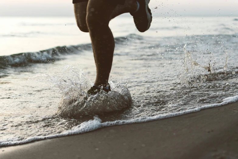 a man riding a surfboard on top of a sandy beach, a picture, unsplash, renaissance, running shoes, splashing water, in the evening, close - up photo