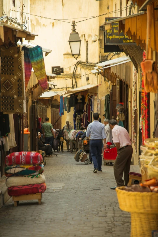 a group of people walking down a street, moroccan, shady alleys, rugs, shops
