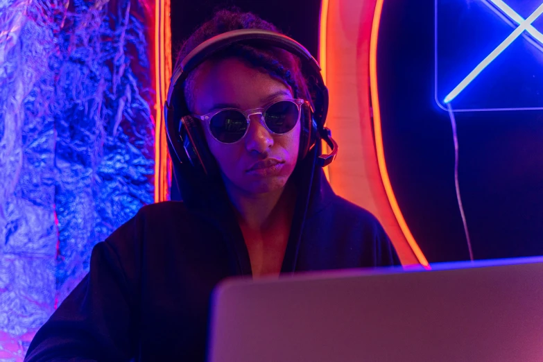 a woman sitting in front of a laptop wearing headphones, pexels, afrofuturism, dj at a party, dark shades, red and blue neon, ashteroth