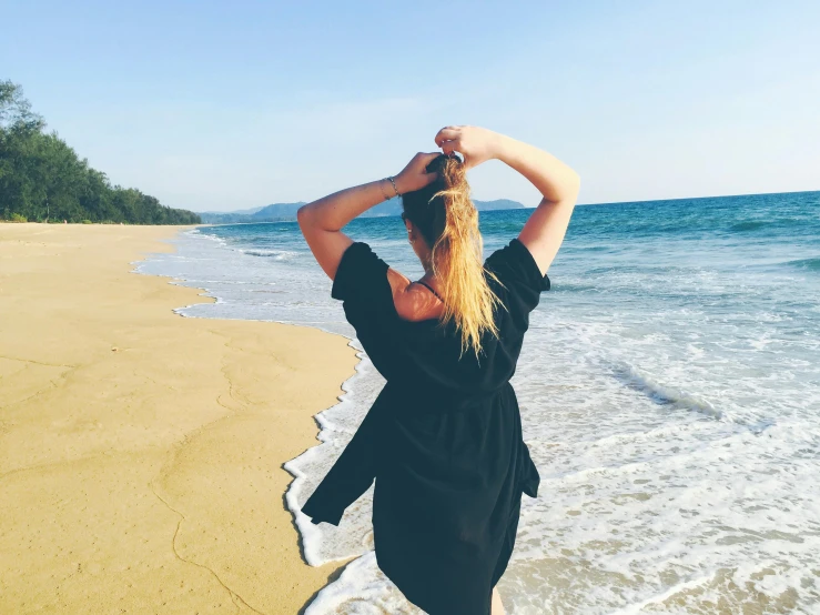 a woman standing on top of a beach next to the ocean, profile image, blonde, splashing, standing with her back to us