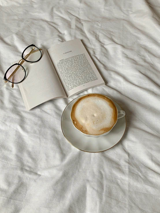 a cup of coffee and a book on a bed, by Rebecca Horn, gucci glasses, instagram story, clean minimalist design, cappuccino