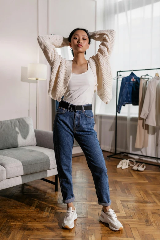 a woman standing in a living room next to a couch, inspired by Jean Hey, trending on pexels, renaissance, outfit : jeans and white vest, with arms up, casual streetwear, met collection