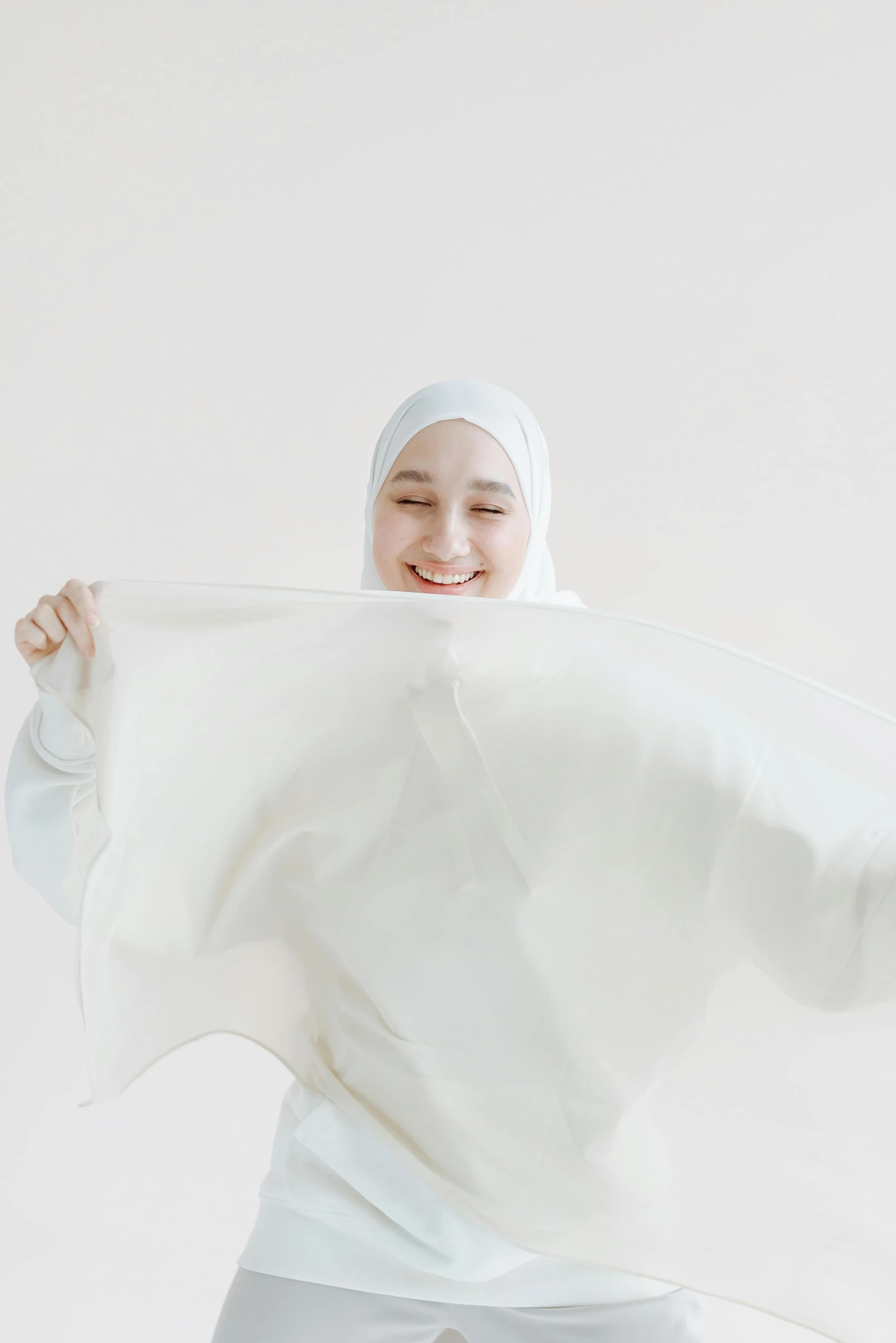 a woman in a white hijab poses for a picture, by Basuki Abdullah, unsplash contest winner, hurufiyya, cream white background, made of lab tissue, expressing joy, made of fabric