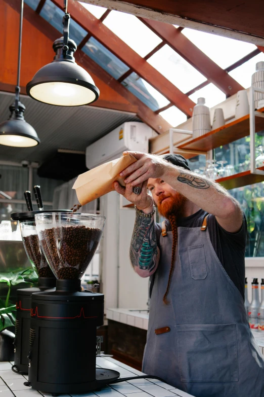 a man in an apron pours coffee into a blender, by Jessie Algie, pexels contest winner, aussie baristas, lush surroundings, gif, tattooed