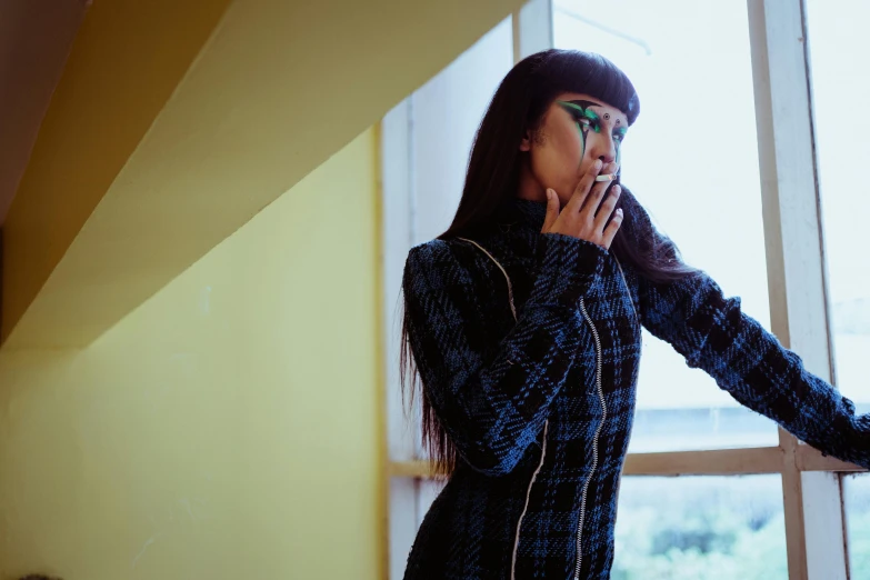 a woman standing in front of a window talking on a cell phone, an album cover, trending on pexels, visual art, black bangs, with teal clothes, patterned clothing, hand over mouth