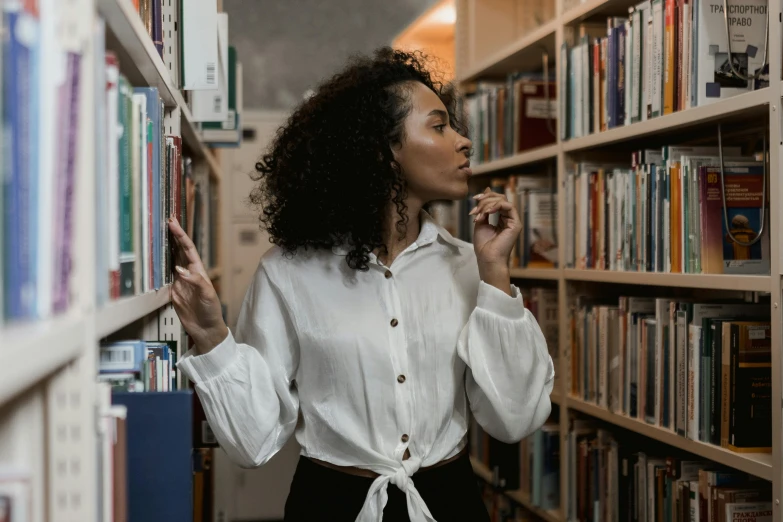 a woman standing in front of a bookshelf in a library, pexels contest winner, wearing a white button up shirt, black female, trending photo, curly haired