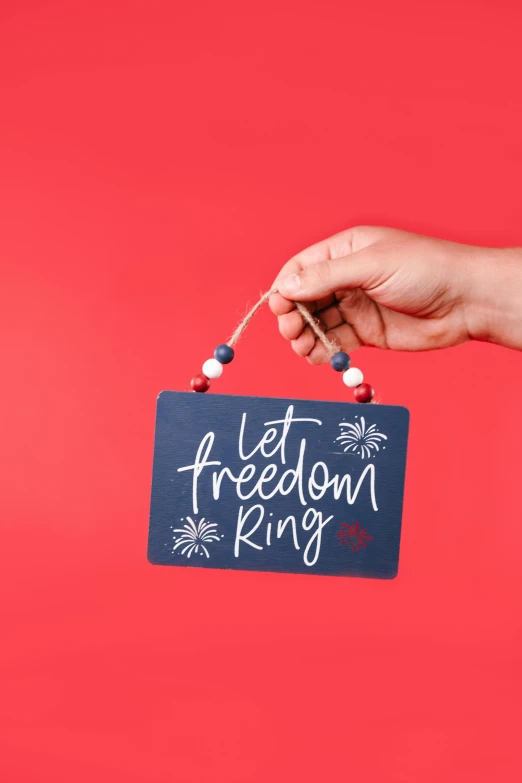 a hand holding a sign that says let freedom ring, by Julia Pishtar, ornament, navy, - 6, carefree