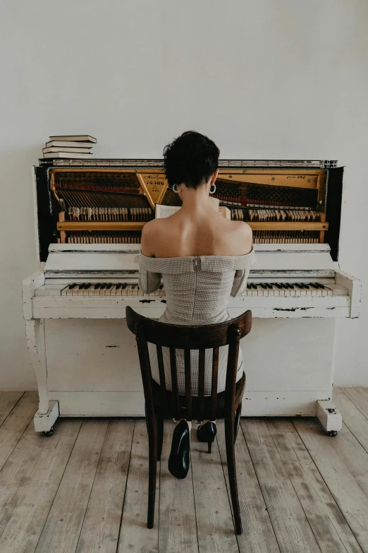 a woman sitting on a chair in front of a piano, on a white table, portrait featured on unsplash, from back, dressed in a worn