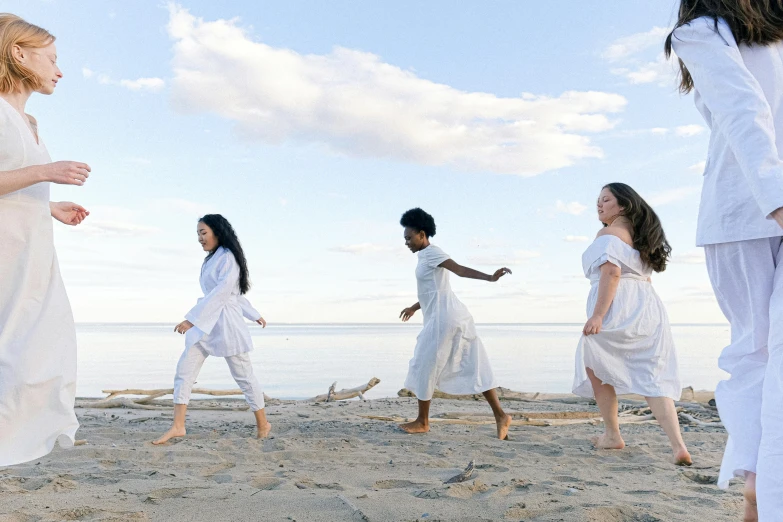 a group of people standing on top of a sandy beach, girl in white dress dancing, triad of muses, inuit heritage, promo image