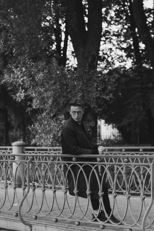 a black and white photo of a man sitting on a bench, inspired by Eliseu Visconti, standing astride a gate, william gibson, photo courtesy museum of art, during autumn
