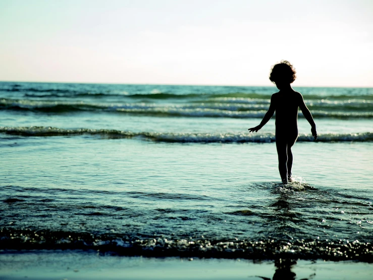 a little boy that is standing in the water, an album cover, unsplash, girl on the beach, silhouette :7, australian beach, high-resolution