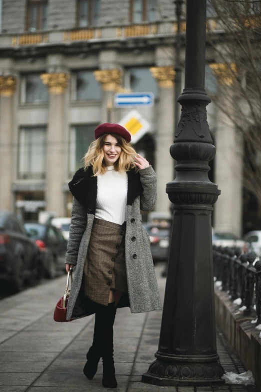 a woman walking down a sidewalk next to a lamp post, a portrait, inspired by Albert Paris Gütersloh, trending on pexels, renaissance, russian clothes, wearing a beret, grey skirt, square