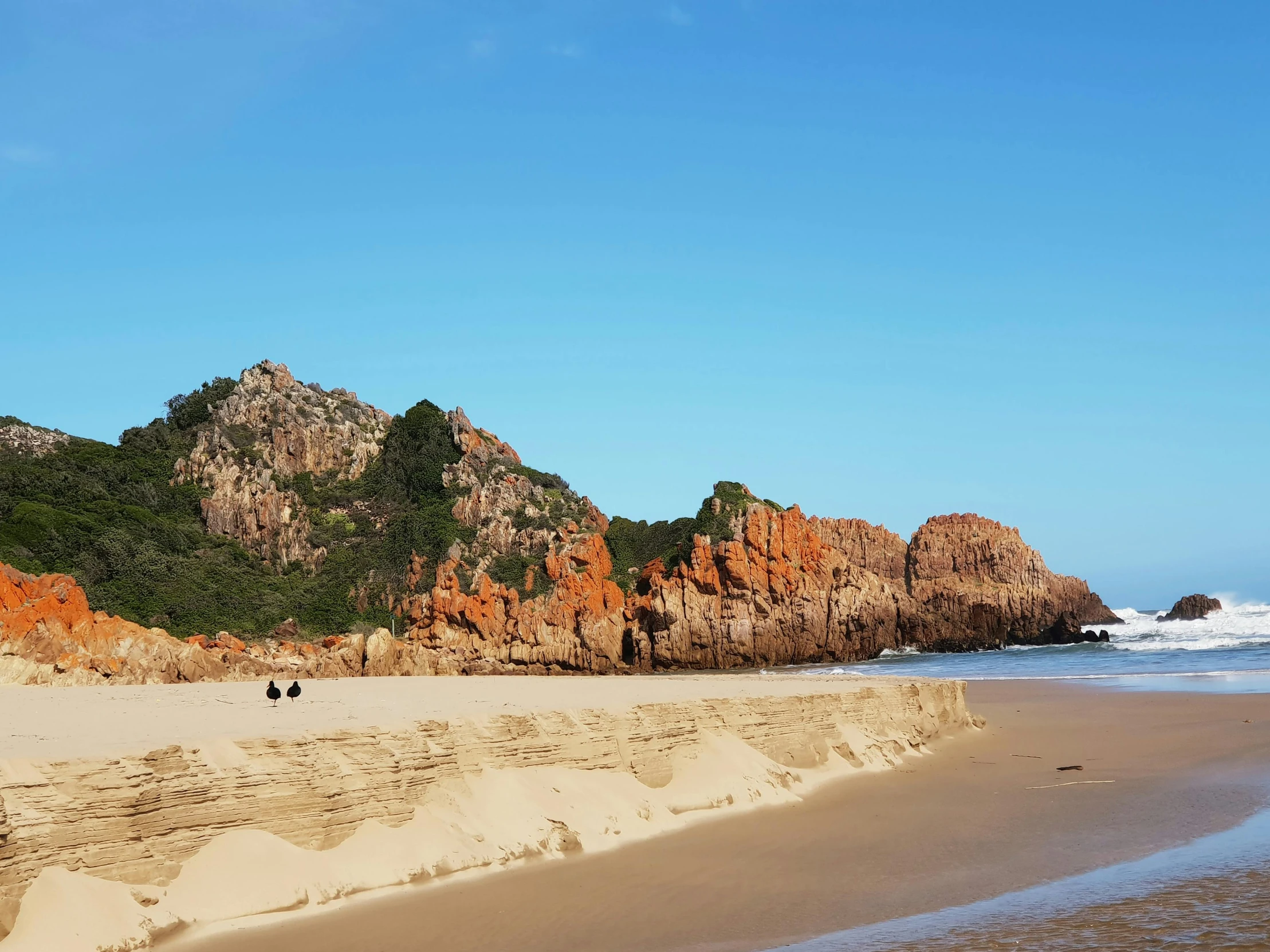 a group of people standing on top of a sandy beach, coastal cliffs, piroca, clear blue skies, red sand