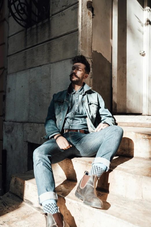 a man sitting on the steps of a building, wearing double denim, pompadour, brightly lit, photo of a model