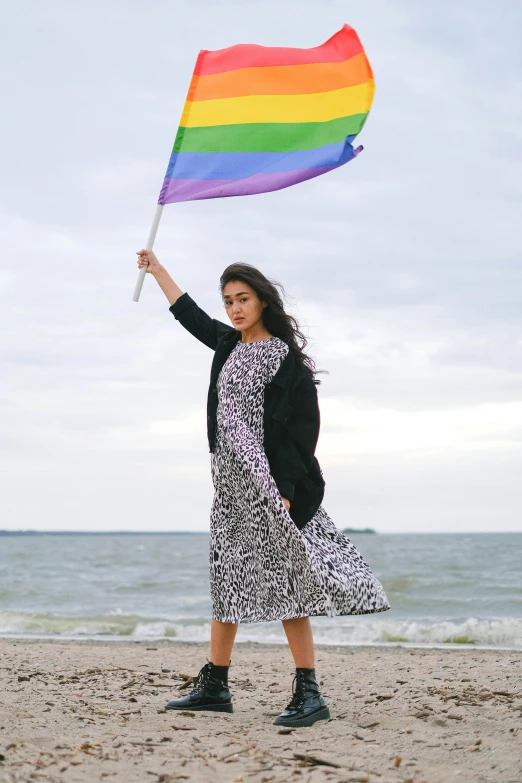 a woman holding a rainbow flag on the beach, a portrait, unsplash, renaissance, patterned clothing, waving, shohreh aghdashloo, non binary model