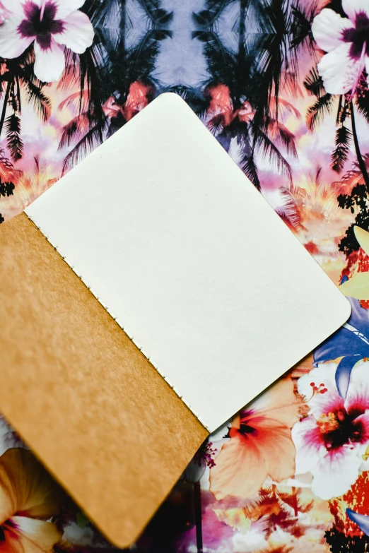 a notebook sitting on top of a bed covered in flowers, by Robbie Trevino, unsplash, tropical style, low quality photo, rough paper texture, bottom - view