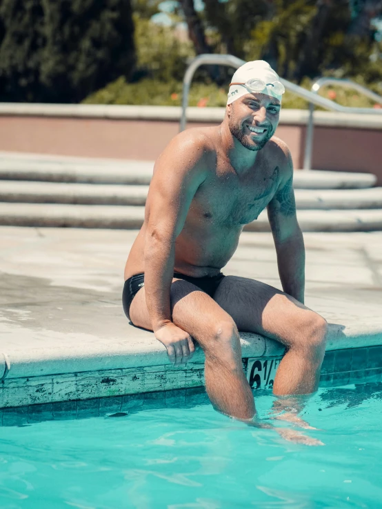 a man sitting on the edge of a swimming pool, smiling spartan, profile image, asher duran, swim suite