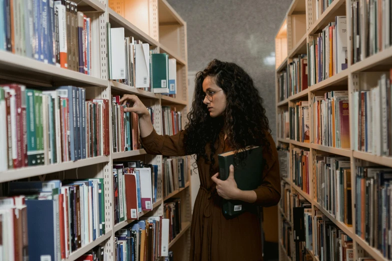 a woman picking a book from a shelf in a library, pexels contest winner, brown curly hair, casually dressed, ameera al-taweel, leaked image