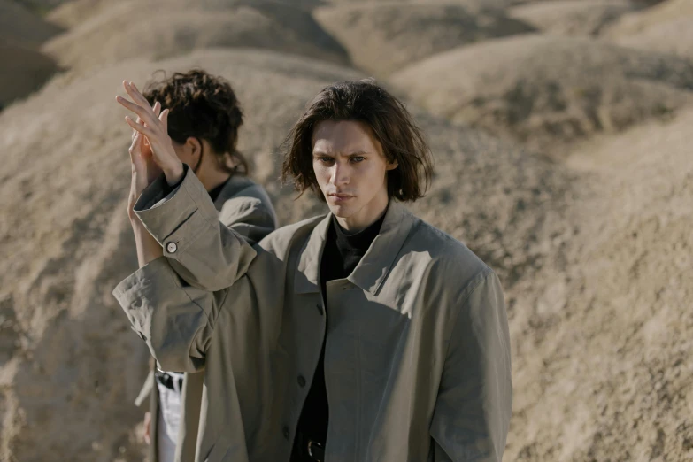 a couple of people that are standing in the dirt, an album cover, unsplash, bauhaus, trench coat, paul atreides, in the desert beside the gulf, ville valo