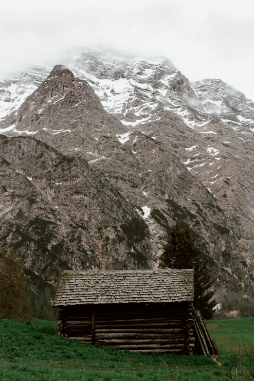 a cabin in a field with a mountain in the background, a picture, inspired by Peter Zumthor, pexels contest winner, renaissance, snowy italian road, rock roof, towering high up over your view, panoramic