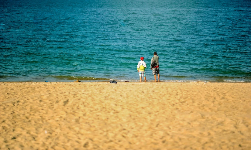a couple of people standing on top of a sandy beach, shallow water, manly, tiny person watching, clean photo