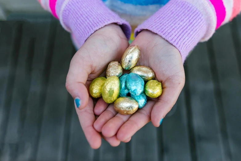 a little girl holding some chocolate eggs in her hands, by Julia Pishtar, pexels contest winner, cyan and gold scheme, made of candy, alex heywood, random metallic colors