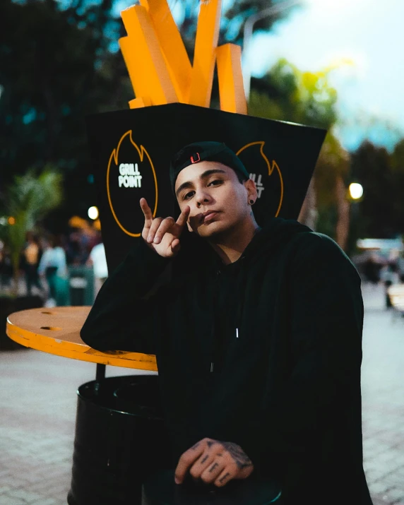 a man sitting next to a trash can with fries on it, an album cover, inspired by Eddie Mendoza, pexels contest winner, graffiti, in black uniform, wreathed in flame, non binary model, headshot profile picture