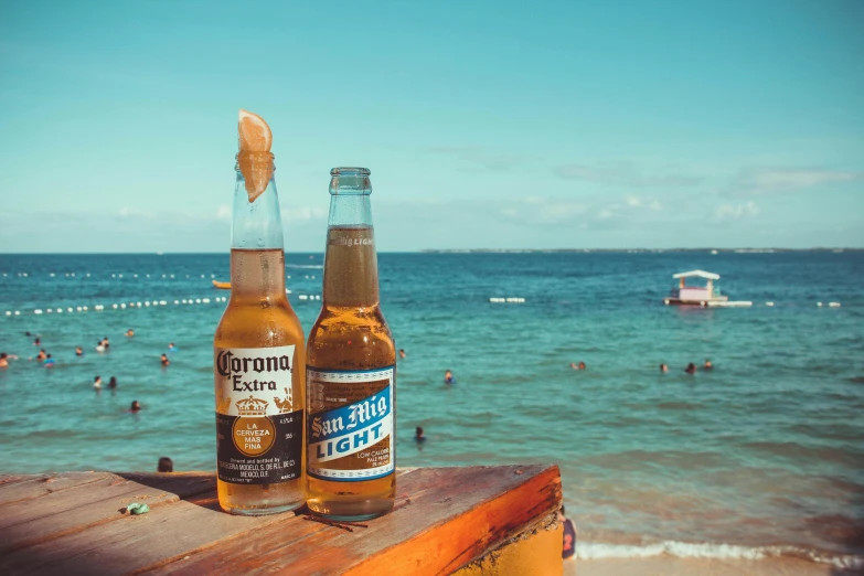 a couple of bottles of beer sitting on top of a wooden table, by Carey Morris, pexels contest winner, light blue water, puerto rico, poster of corona virus, all around