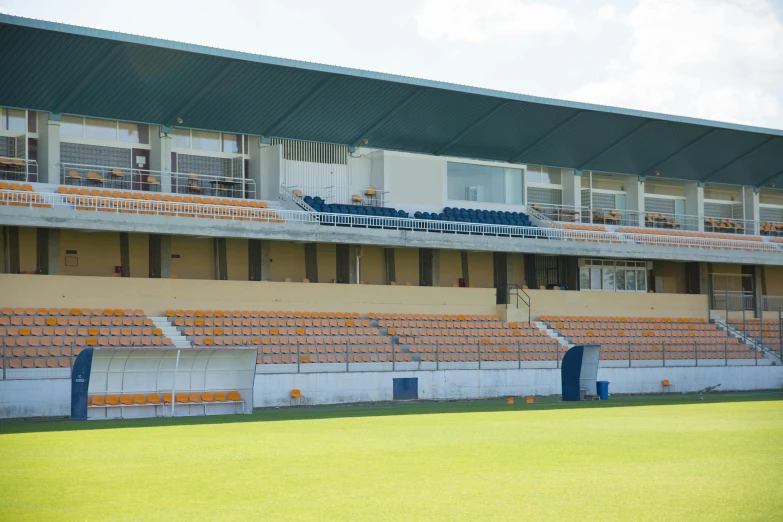 a man standing on top of a lush green field, sportspalast amphitheatre, coloured in blueberra and orange, white and yellow scheme, rows of canteen in background