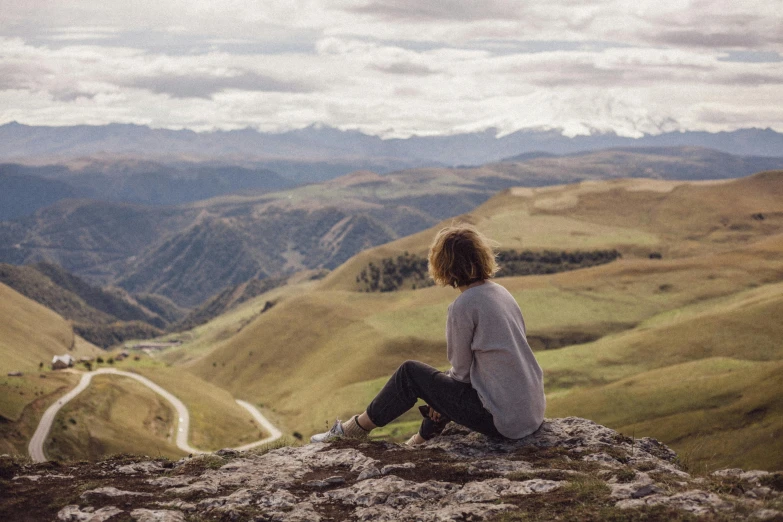 a woman sitting on top of a mountain overlooking a valley, by Anna Findlay, pexels contest winner, visual art, new zeeland, rolling foothills, instagram post, without text