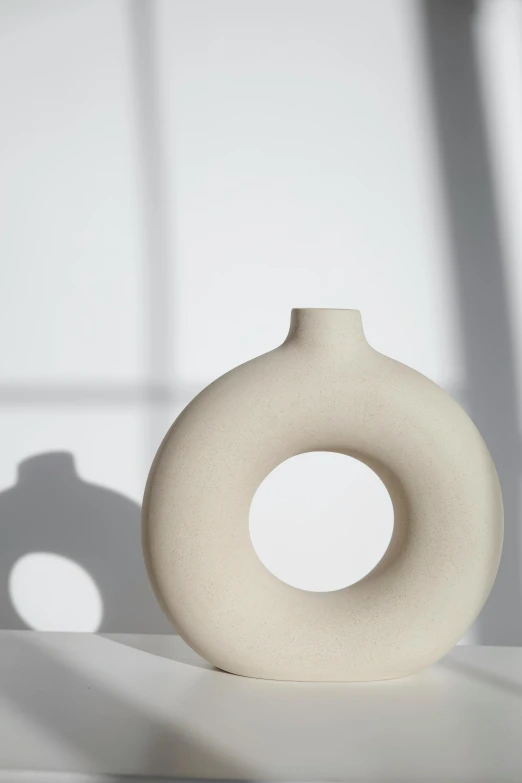 a white vase sitting on top of a table, an abstract sculpture, unsplash, minimalism, round bottle, enso, warm shading, ignant