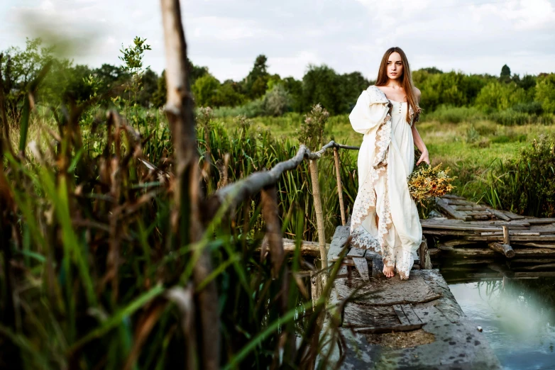 a woman in a white dress standing on a bridge, inspired by Apollinary Vasnetsov, unsplash, renaissance, kirsty mitchell, portrait image, late summer evening, full - length photo