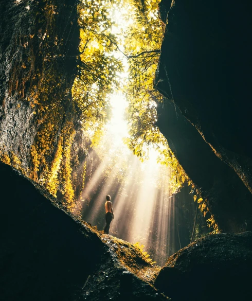a person standing in the middle of a cave, a picture, unsplash contest winner, light and space, sun - rays through canopy, indonesia national geographic, lush mossy canyon, golden hour 4k